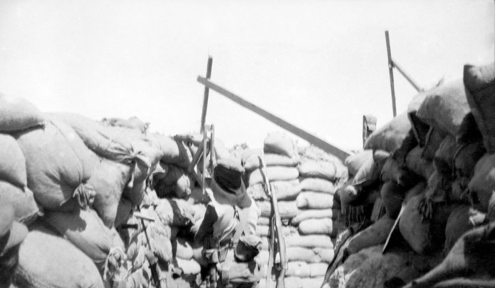 A sniper using a periscope rifle at Quinn's Post. The framework of a wire netting bomb screen is showing.