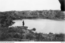 A soldier stands next to a large water-filled mine crater, blown by Australian Engineers at the start of the Battle of Messines, near Wytschaete.