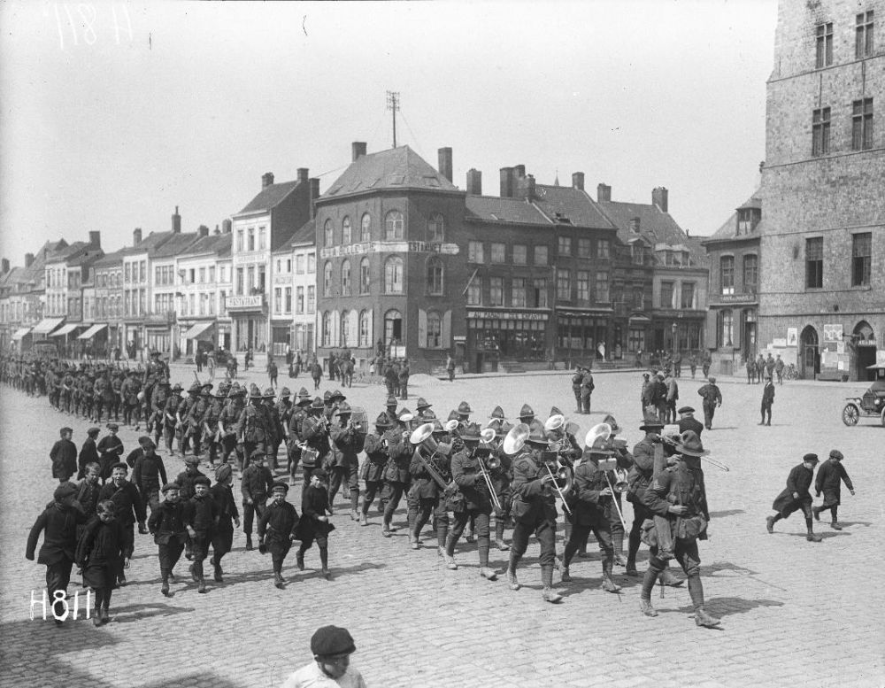 New Zealand soldiers, some playing trombones, trumpets, and drums, marching through Bailleul.